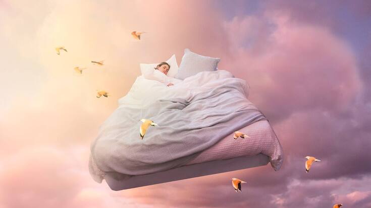 A sleeping girl floats on a bed in the sky 