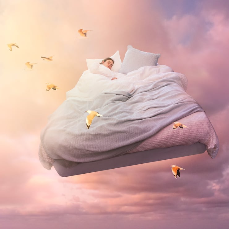 A sleeping girl floats on a bed in the sky 