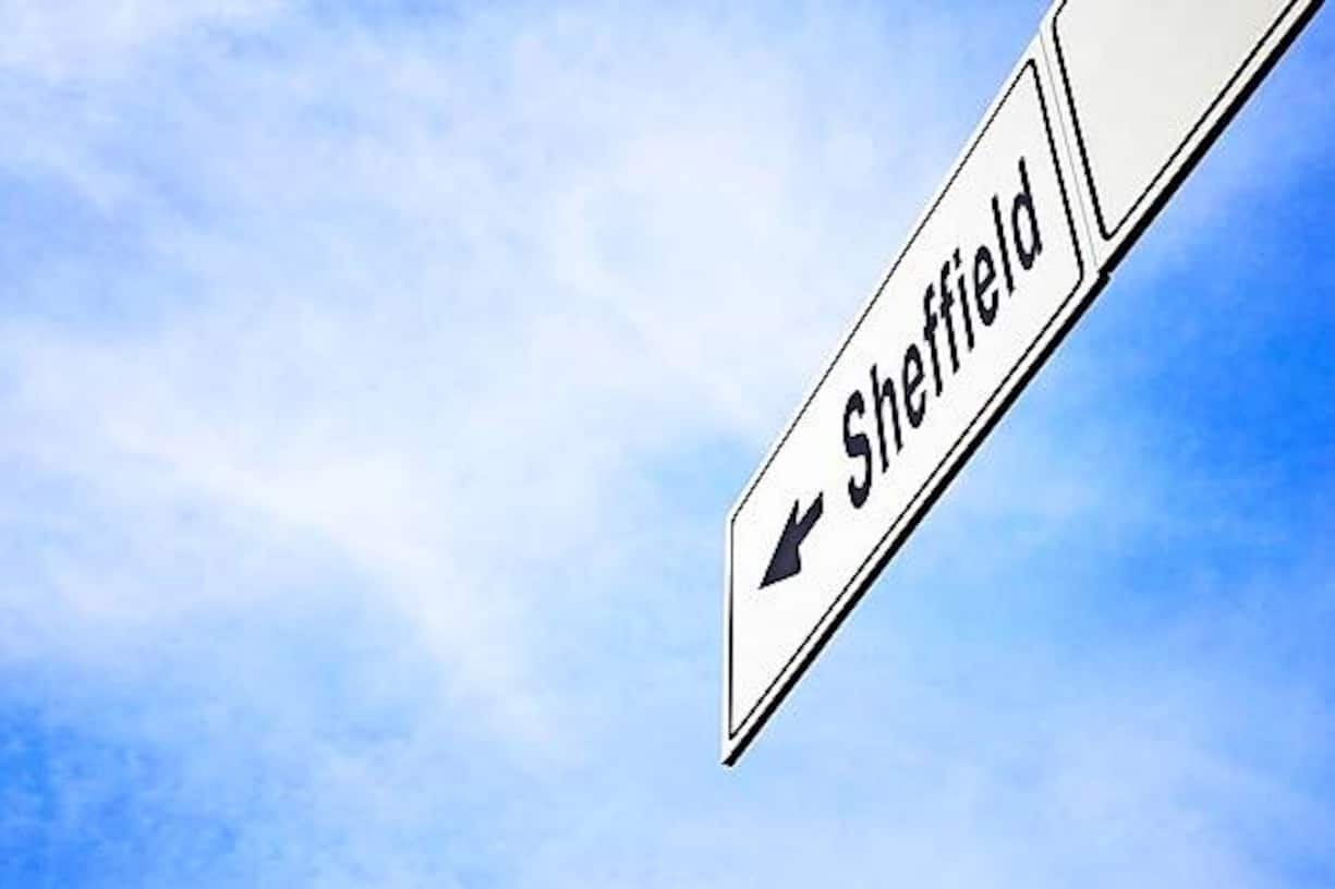 White signboard with an arrow pointing left towards Sheffield, England, United Kingdom, against a hazy blue sky in a concept of travel, navigation and direction